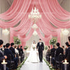 A wedding ceremony setup featuring pink draped curtains, a bride and groom, and guests seated on both sides.