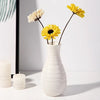A white ceramic vase holds two stems of yellow and white flowers against a light background.
