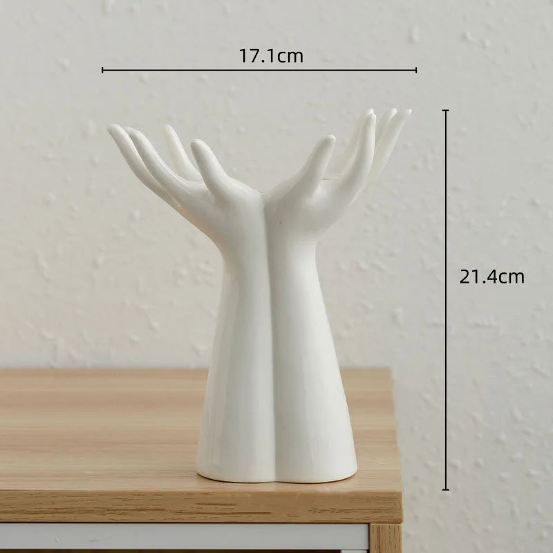 A white ceramic hand sculpture with open fingers, used as a vase or home décor item.