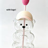 A clear glass coffee cup with a pink strawberry on a stick is held by a bear-shaped clear glass holder.