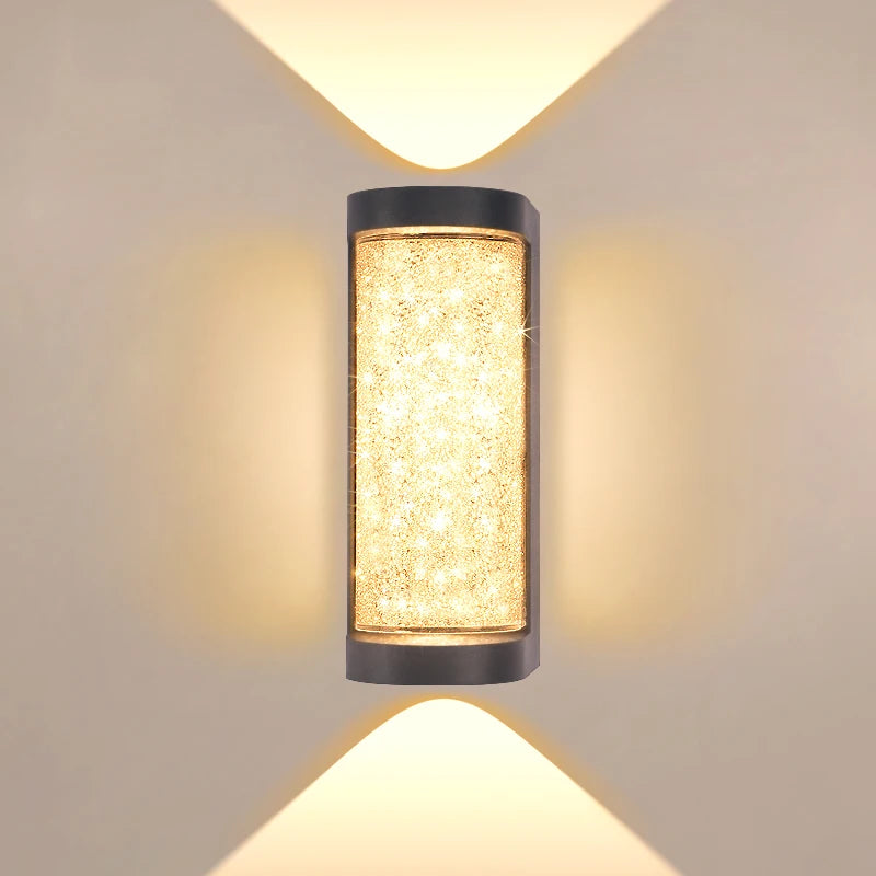 A vertical, cylindrical LED crystal outdoor wall sconce with a warm yellow glow mounted on a light beige wall.