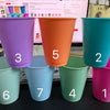 Seven plastic cold cups in various colors including purple, orange, teal, and pink, displayed on a black surface.
