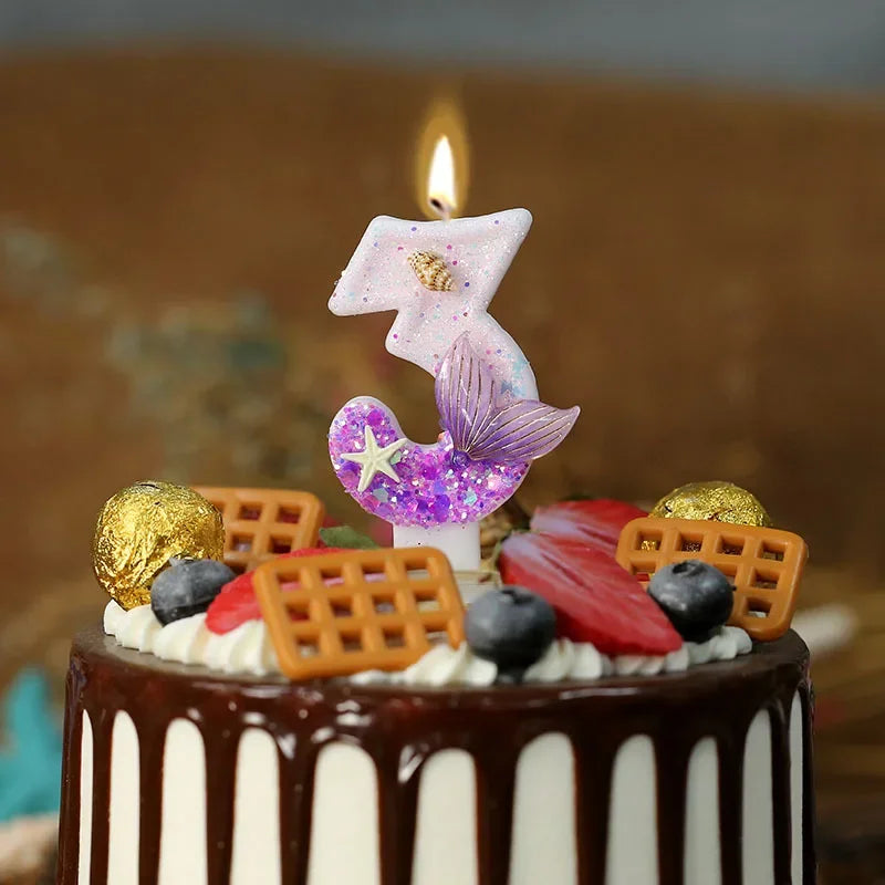 A cake decorated with mermaid tail candles and various fruit and cookie accents, lit by a flame.