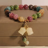 A bracelet made of various colored natural stones, including pinks, greens, and browns, displayed on a wooden box.