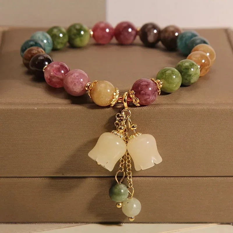 A bracelet made of various colored natural stones, including pinks, greens, and browns, displayed on a wooden box.