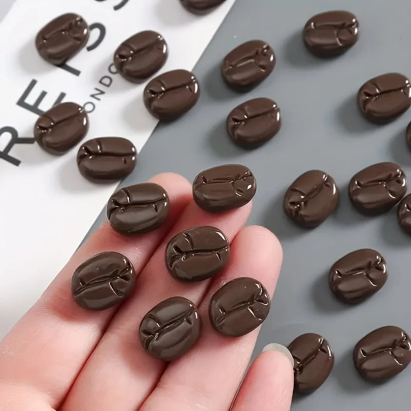 Une main tient un ensemble de huit aimants à réfrigérateur réalistes en grains de café brun foncé sur un fond gris.