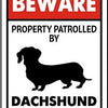 A red and white warning sign that says BEWARE PROPERTY PATROLLED BY DACHSHUND SECURITY