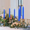 A display of tall blue stick candles in a floral arrangement on a white surface.