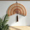 Handwoven bamboo wall fan decor with a light brown and beige striped design and a tassel hanging on a white wall.