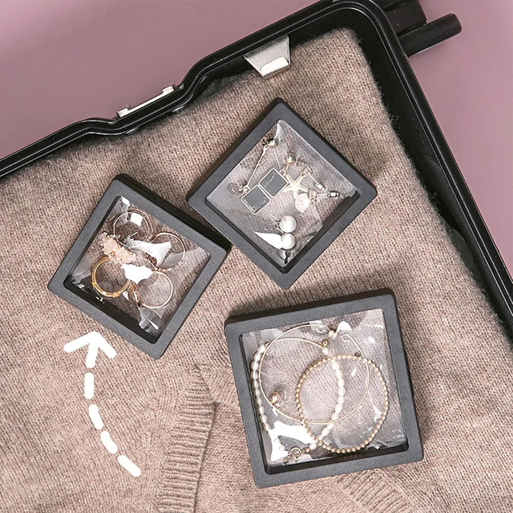 A display of various jewelry pieces in small black shadow boxes resting on a beige fabric.