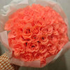 A bouquet of vibrant orange-pink silk roses wrapped in sheer white paper.
