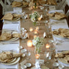 A table setting featuring natural beeswax tealight candles, linen napkins, and glassware for ambiance.