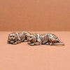 A vintage brass tiger figurine statue lying down on a neutral brown surface.