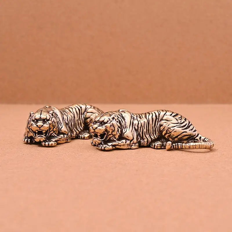 A vintage brass tiger figurine statue lying down on a neutral brown surface.