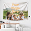A family of three laughing and looking at a photo on a large tapestry featuring the text Your Image Here