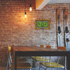 A vintage metal sign with a green dollar bill and a green leaf displayed on a brick wall above a wooden table.