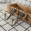 A pair of vintage crown curtain hooks with decorative metalwork resting in a wooden box on a checkered surface.