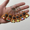 Une main tient plusieurs pendentifs de clés à:=\ capybara bruns avec accents colorés et chaînes argentées.
