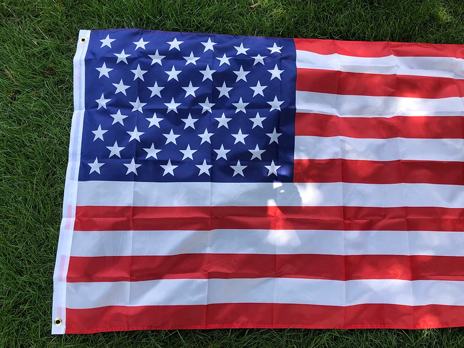 A large American flag displayed flat on green grass.