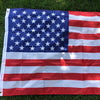 A large American flag displayed flat on green grass.
