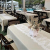 White embroidered lace table runner on a white tablecloth set for an outdoor wedding event.