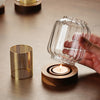 A hand holds a vintage wooden candle lantern with a glass cover next to a small brass decorative container.