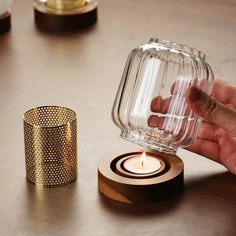A hand holds a vintage wooden candle lantern with a glass cover next to a small brass decorative container.