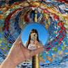 Eine Hand hält einen tragbaren konvexen Selfie-Spiegel, der den Himmel und farbige Fallschirmgewebe reflektiert.