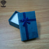 Caja de regalo rectangular de terciopelo azul atada con una cinta azul oscuro, sobre una superficie de madera.