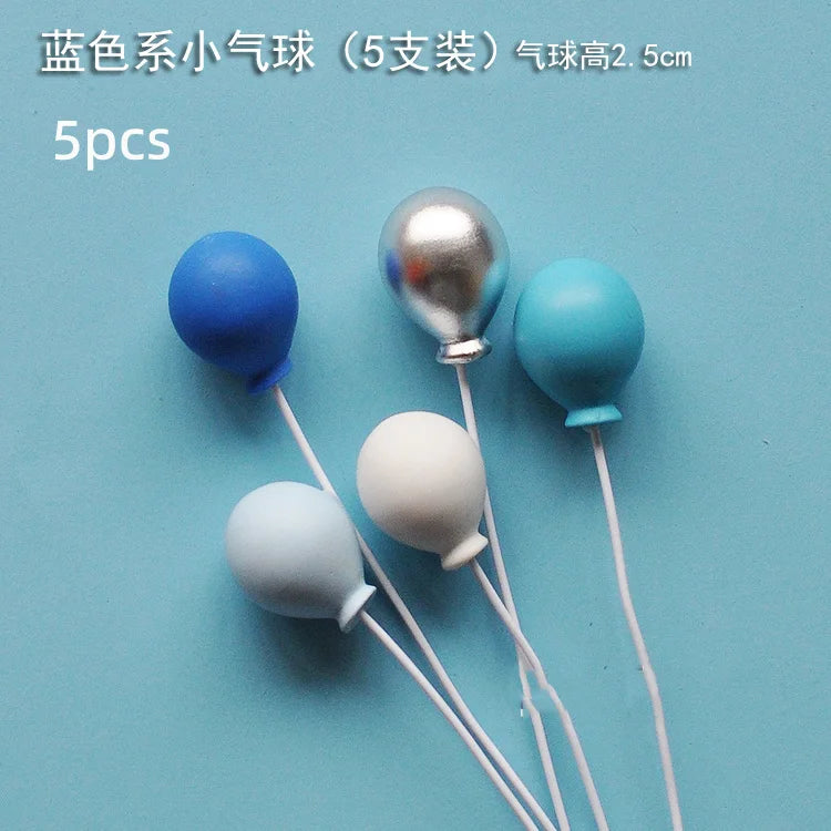 Five balloons in various colors including blue, silver, and light blue, with thin strings.