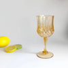 A clear, textured glass wine goblet with a stem and foot sits on a white surface next to a yellow lemon and a lime slice.