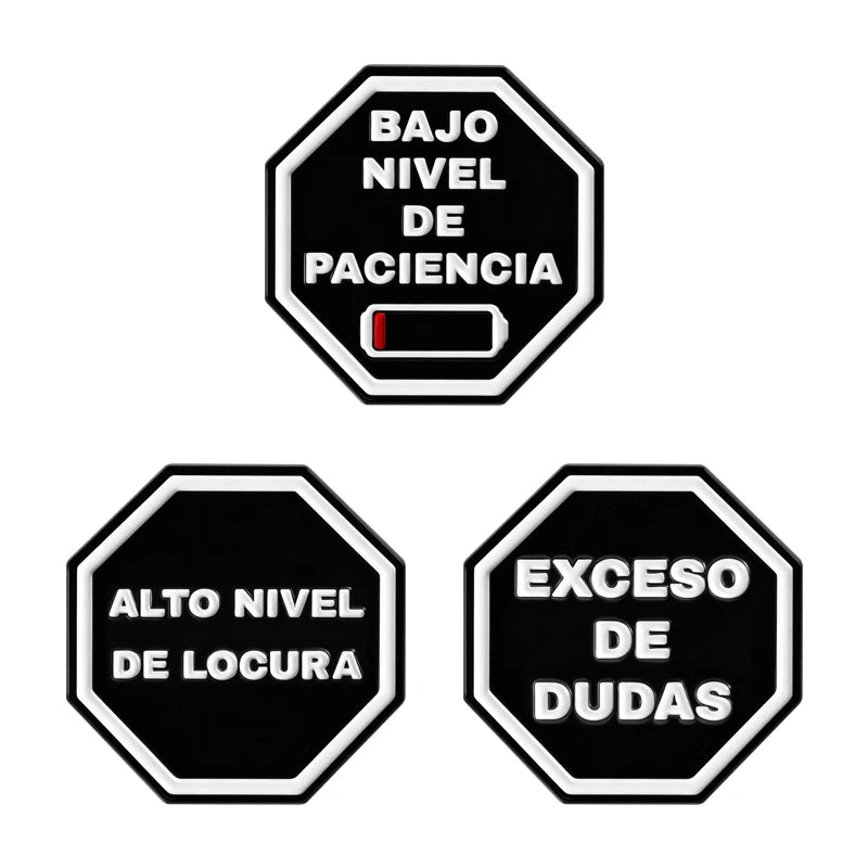 Two black hexagonal enamel pins showing 'BAJO NIVEL DE PACIENCIA' and 'EXCESO DE DUDAS'