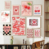 A gallery wall display featuring pink and red floral art prints with hearts and bows on a white wall.