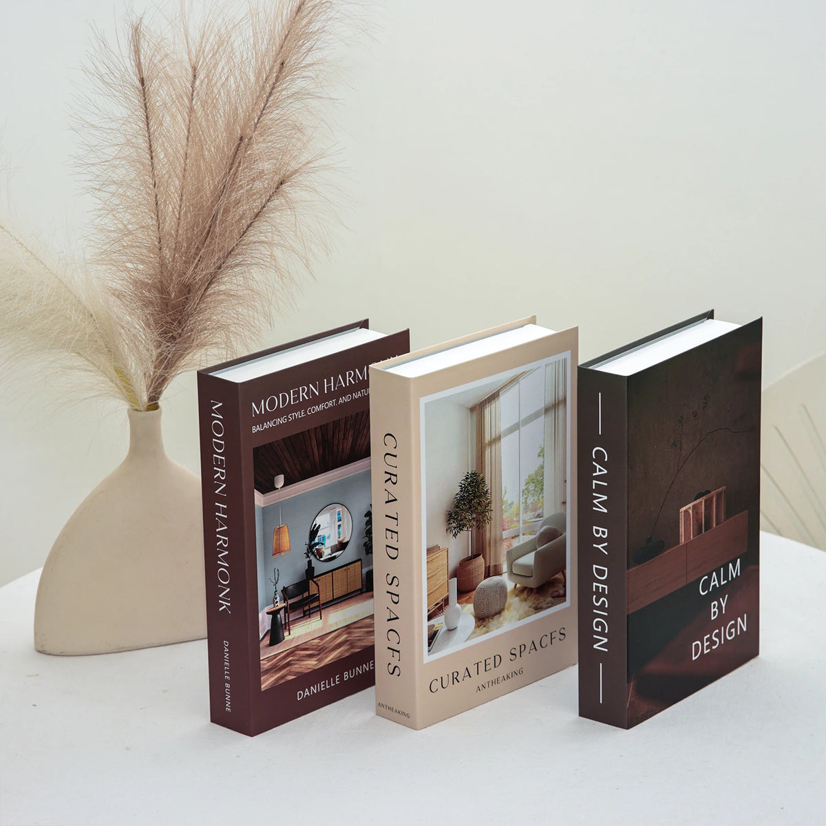 A set of three modern hardcover books titled Modern Harmonk, Curated Spaces, and Calm by Design displayed on a white surface.