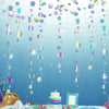 Iridescent mermaid and jellyfish party streamers hanging against a blue background with a cake.