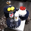A decorative buffet riser set featuring dark blue geometric stands holding a bottle of Malibu and a strawberry cake.