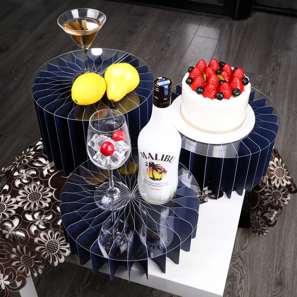 A decorative buffet riser set featuring dark blue geometric stands holding a bottle of Malibu and a strawberry cake.
