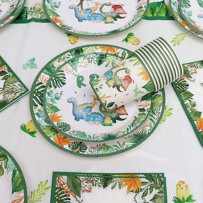 A green and white dinosaur-themed disposable tableware set featuring plates, a banner, and balloons on a white tablecloth.