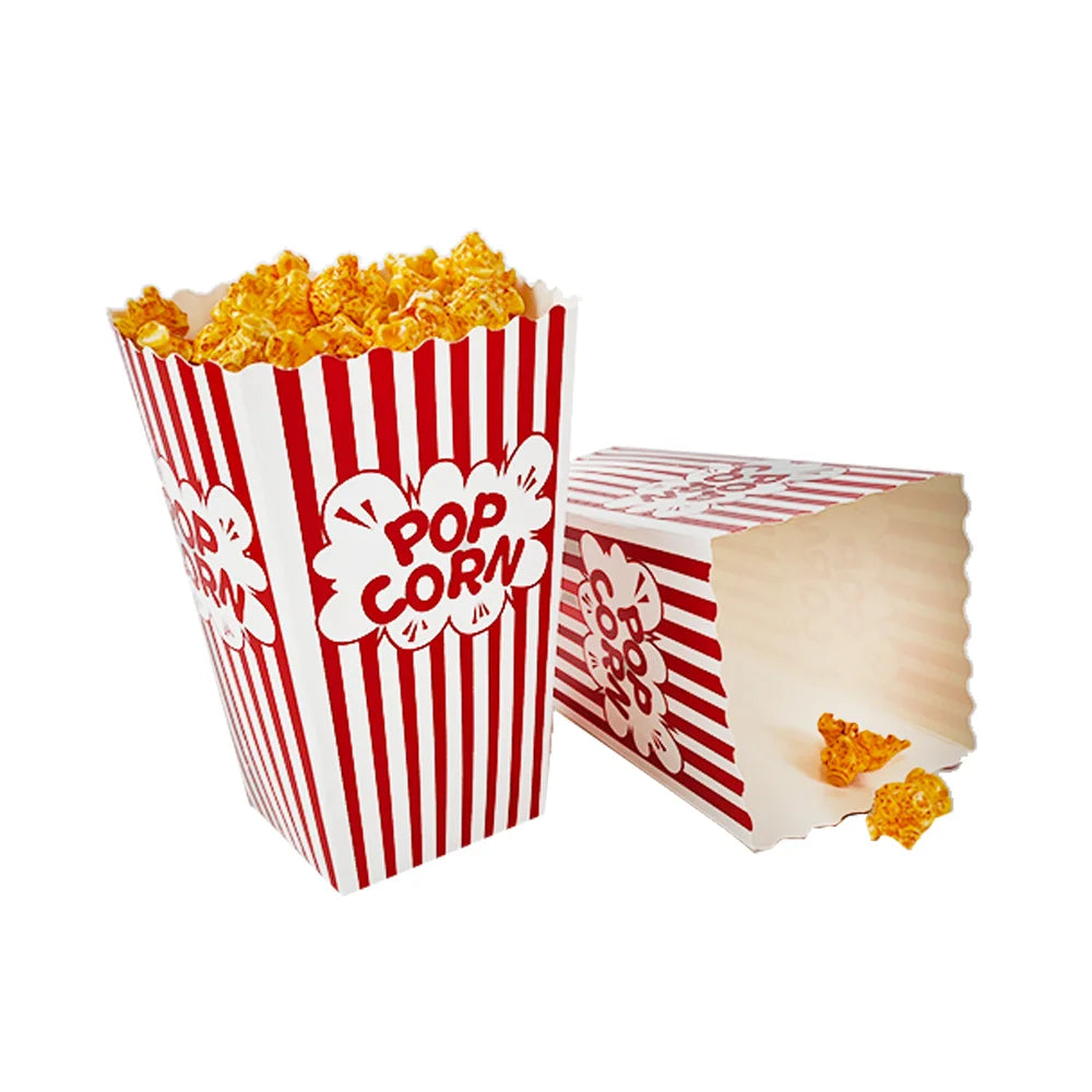 A white paper box with red stripes filled with popped corn, next to a loose piece of popcorn.