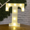 A glowing warm white LED alphabet letter light shaped like the letter T resting on a wooden surface.