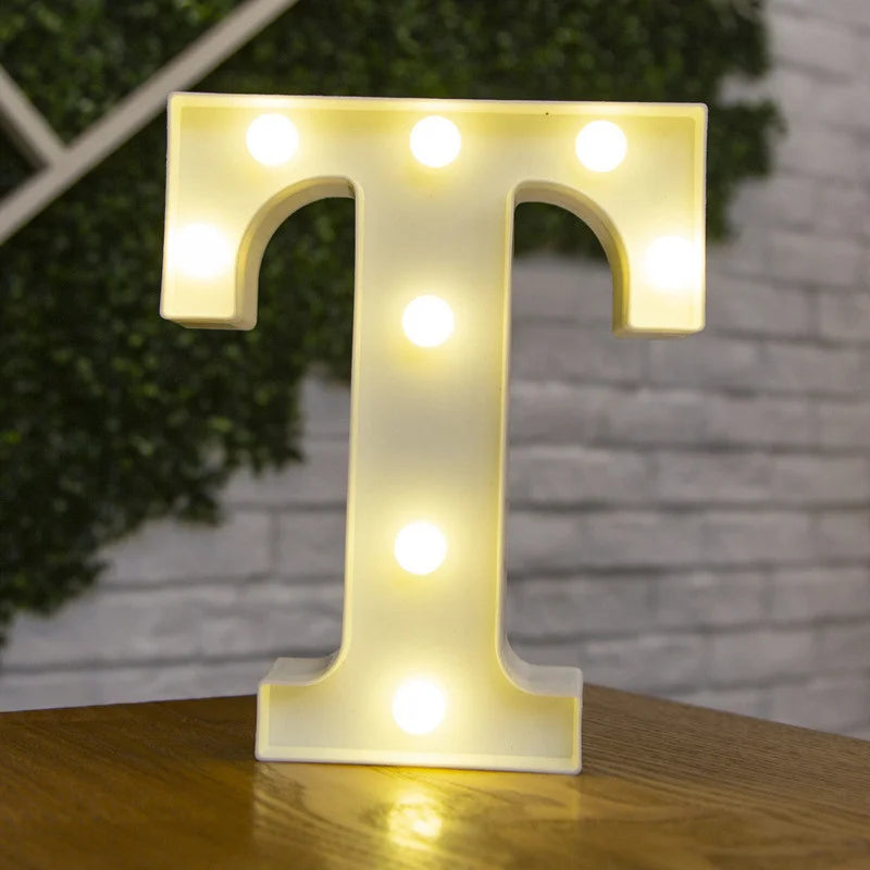 A glowing warm white LED alphabet letter light shaped like the letter T resting on a wooden surface.