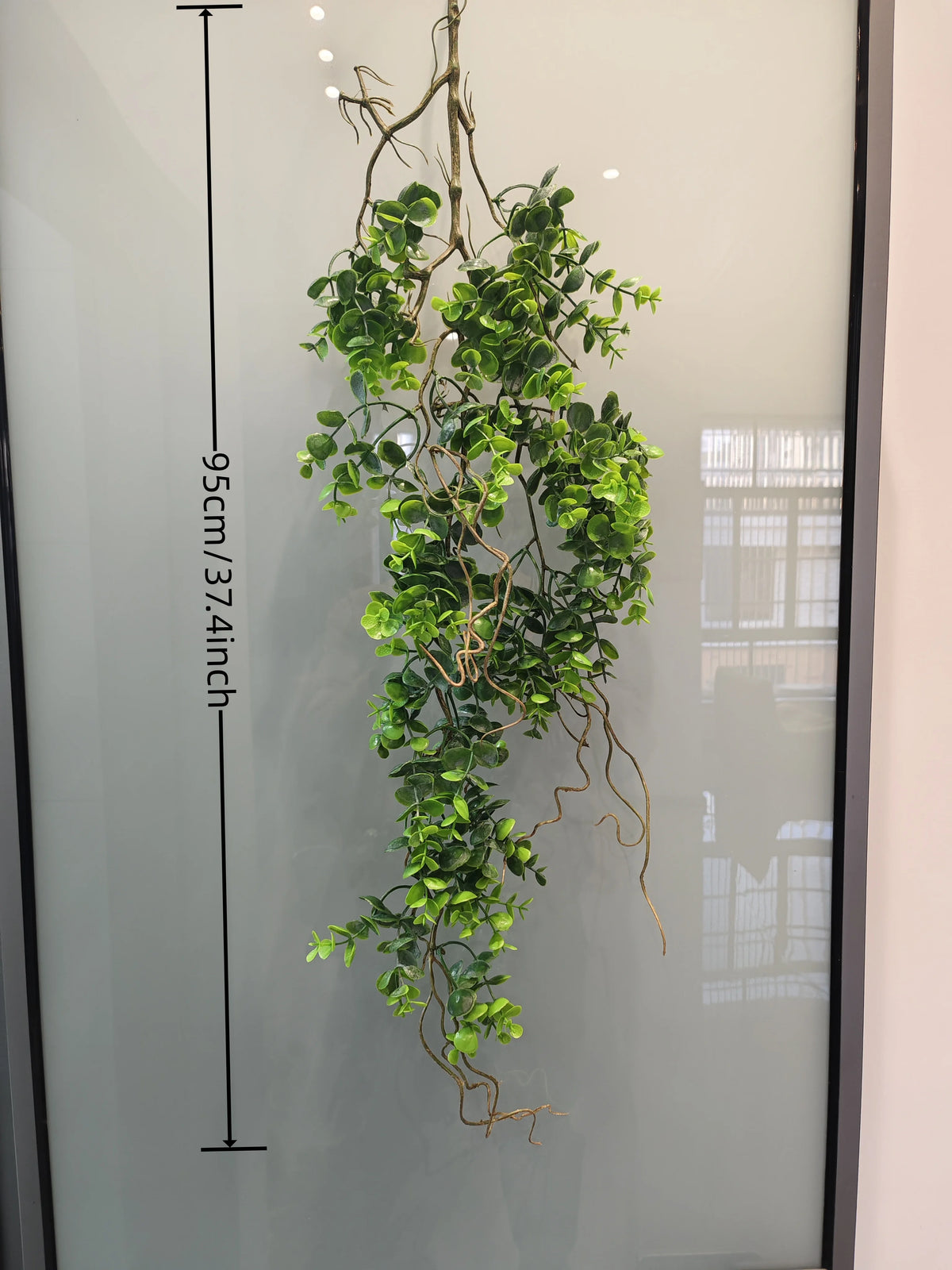 Artificial hanging ivy vine with green leaves displayed against a glass panel.