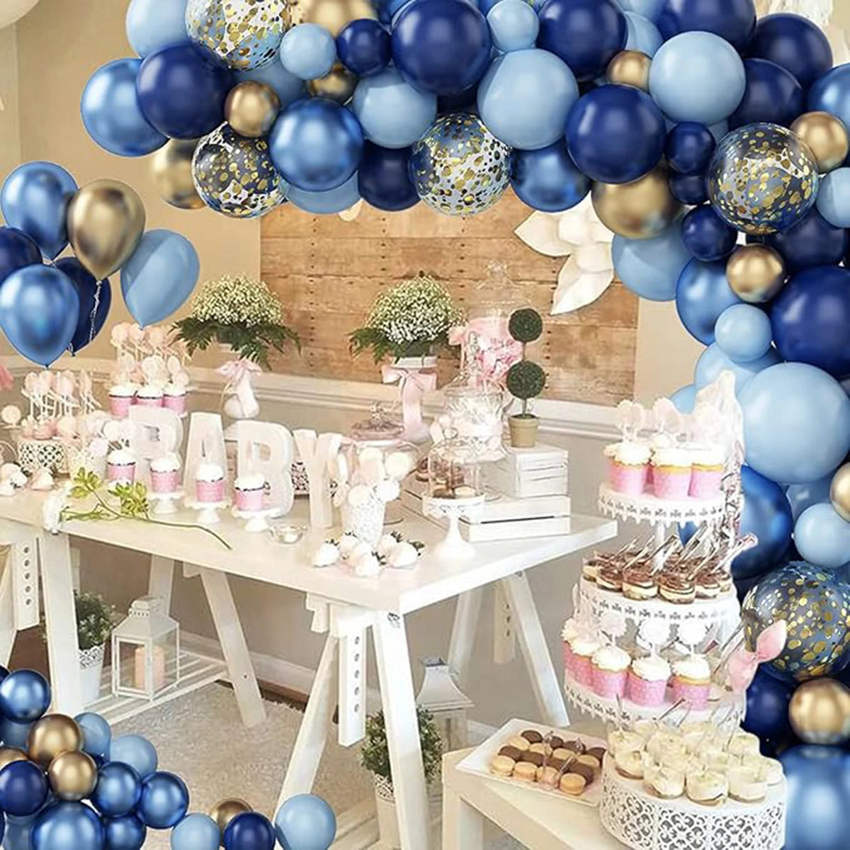 A display of metallic blue and gold balloons, confetti, and sweets arranged for a party decoration.