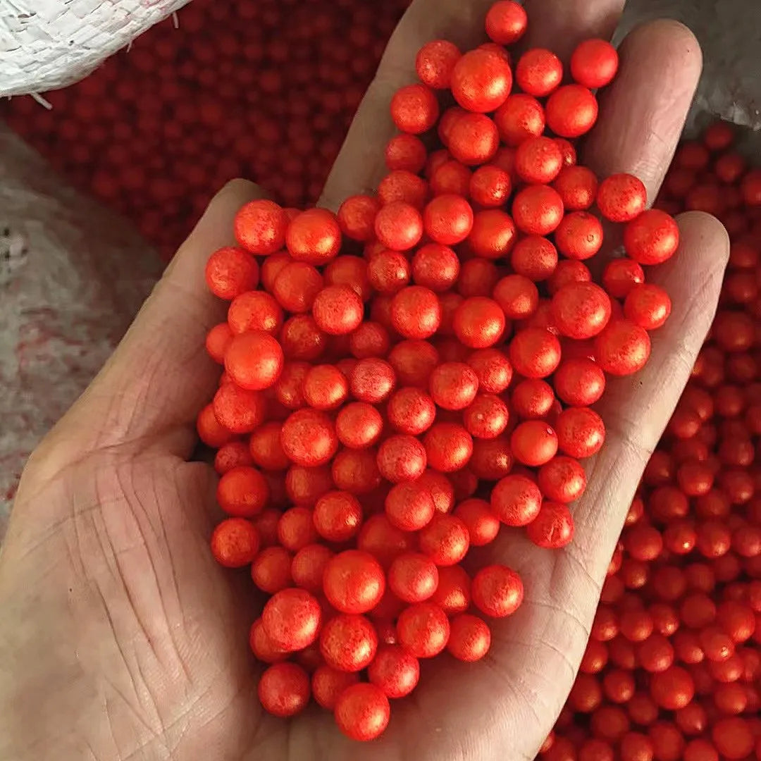 A hand holds a large pile of bright orange foam beads for crafting and decoration.