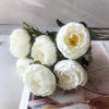 A bouquet of white silk rose and peony artificial flowers arranged on a light surface.
