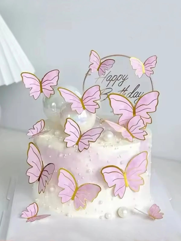 A white cake decorated with pink butterfly toppers and a gold circle sign reading Happy Birthday