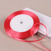 A spool of bright red satin ribbon lying next to a white rectangular object.