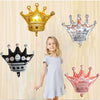 A young girl stands below three foil crowns: gold, silver, and rose gold, against a light background.