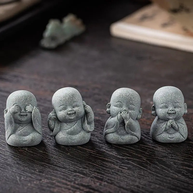 Four small gray stone monk statues in meditation poses arranged on a dark wooden surface.