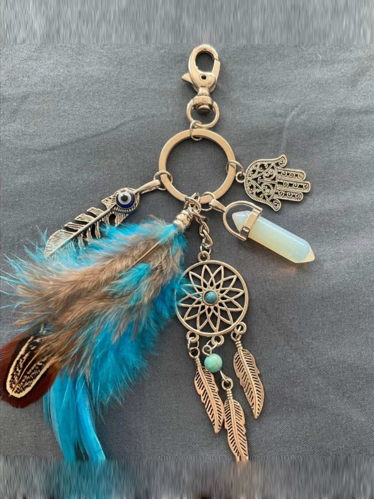 A bohemian dream catcher keychain featuring a feather, tassel, and light green bead on a gold-toned metal chain.